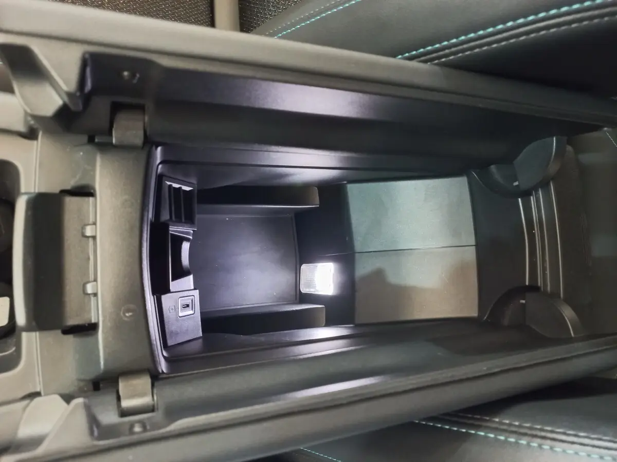 Vue en plongée de la console centrale ouverte de la Peugeot 308 bleu, montrant un espace de rangement avec port USB intégré.