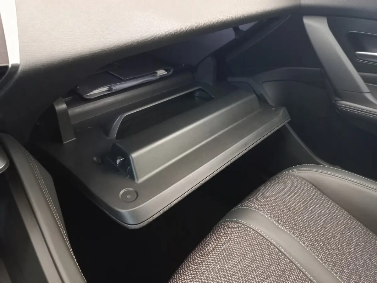 Intérieur de la Peugeot 308 2022, vue côté passager sur la boîte à gants ouverte et siège tissu gris.