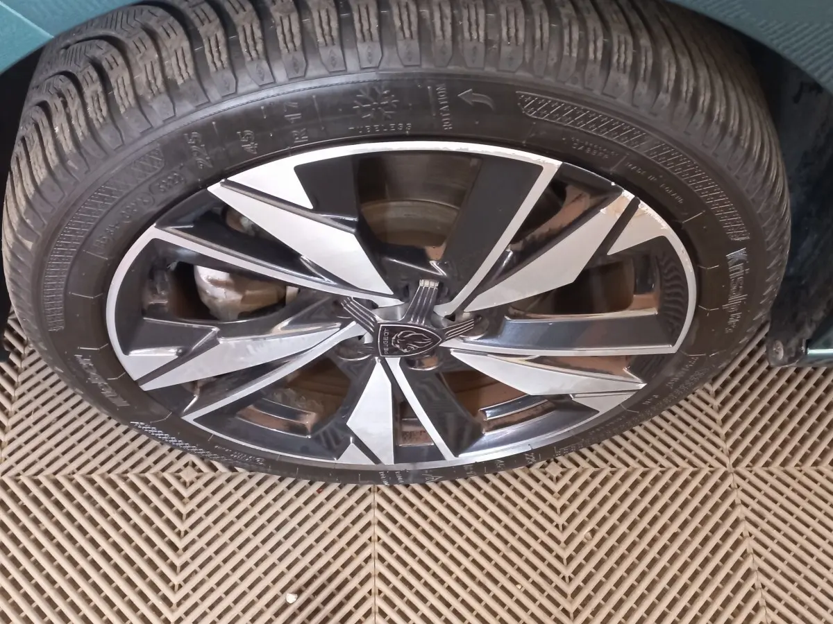 Gros plan sur la jante alliage bicolore noire et argentée d'une Peugeot 308 bleu 2022, vue de dessus.