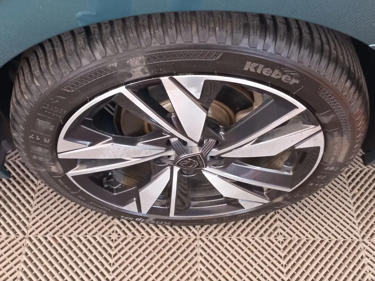 Gros plan sur la roue avant droite d’une Peugeot 308 bleu, jante alliage bicolore au design moderne.