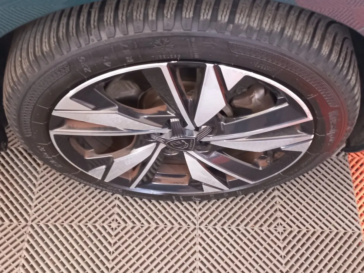 Gros plan sur la jante alliage noire et argentée d’une Peugeot 308 bleu, mettant en valeur le logo central.