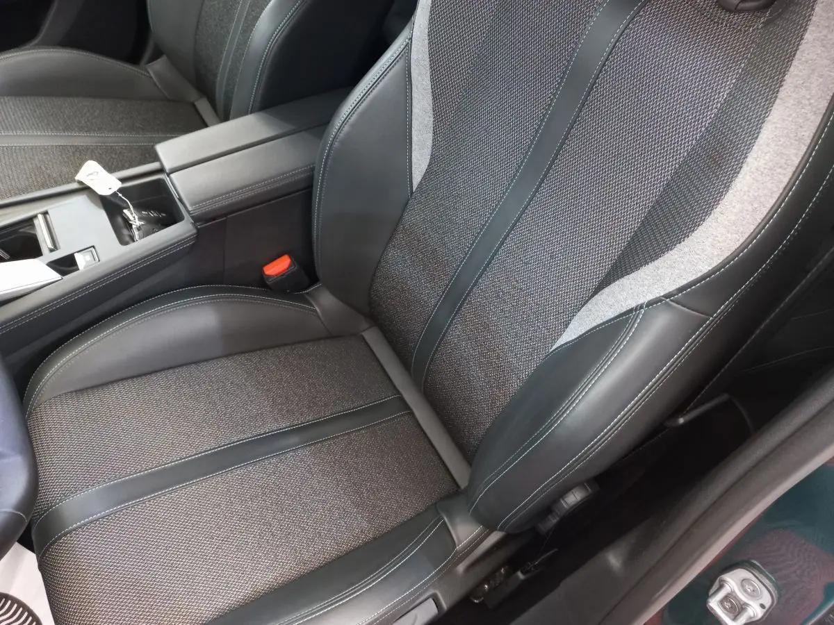 Gros plan sur le siège avant droit en tissu et cuir noir de la Peugeot 308 bleu, avec accoudoir central visible.