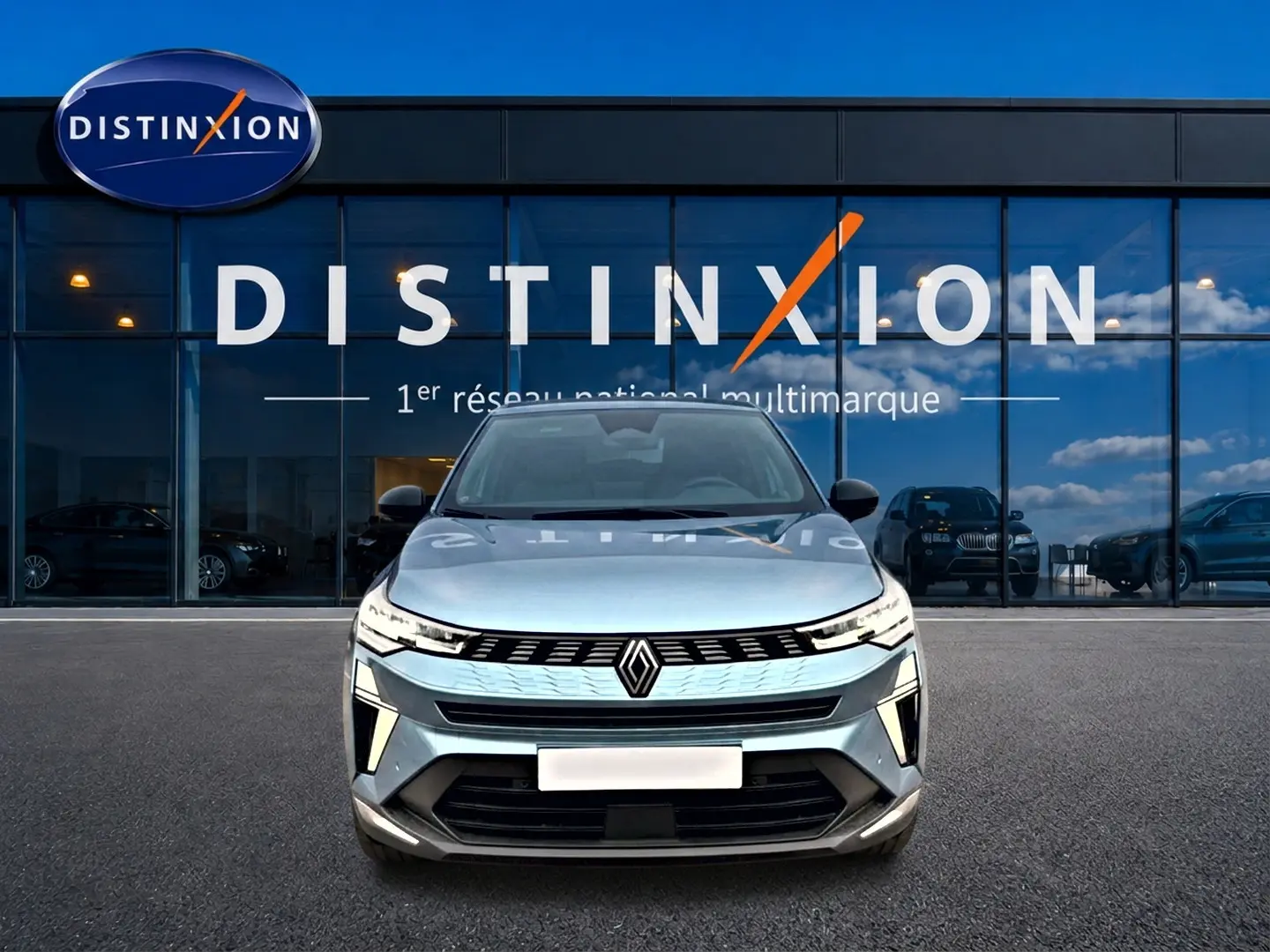Vue avant d'une Renault Symbioz bleu mercure avec calandre lumineuse et logo central devant un showroom Distinxion.