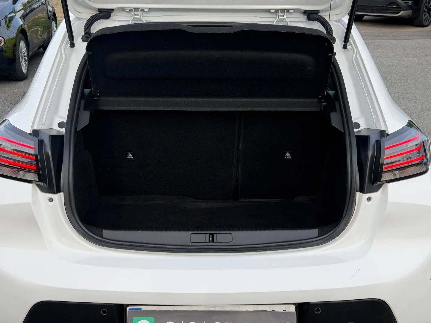 Coffre ouvert vu de l'arrière d'une Peugeot 208 blanche Okénite avec feux arrière LED distinctifs.