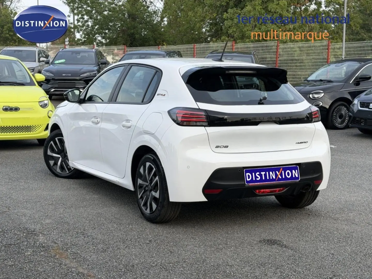 Vue 3/4 arrière droite d'une Peugeot 208 blanche Okénite avec détails noirs et jantes stylisées, stationnée en extérieur.