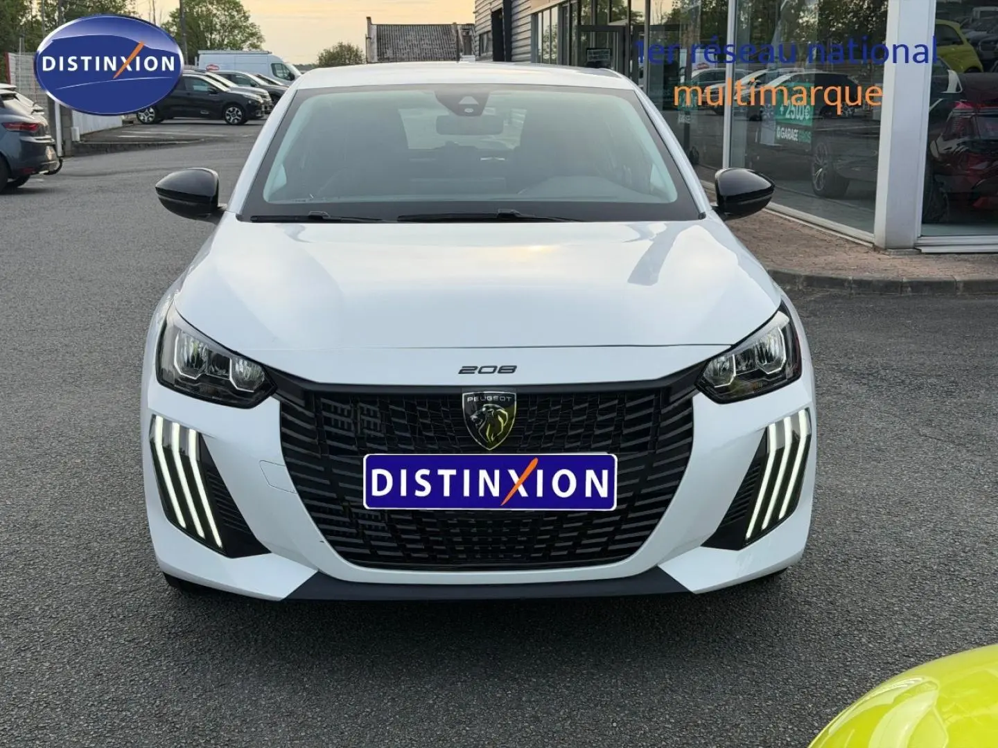 Vue avant d'une Peugeot 208 blanche Okénite avec calandre noire et feux LED verticaux distinctifs allumés.