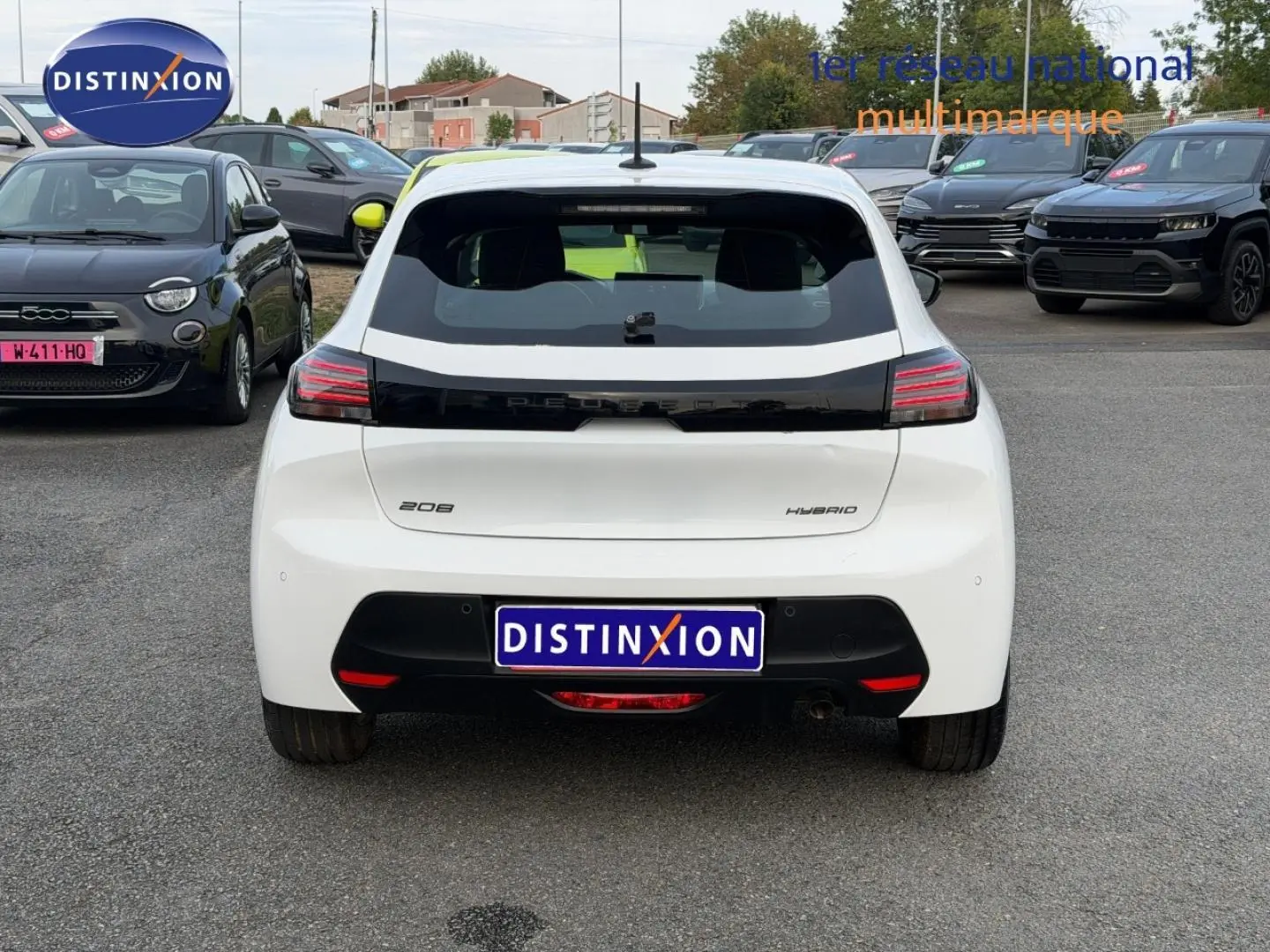 Vue arrière d'une Peugeot 208 hybride blanche Okénite avec feux arrière LED et logo noir brillant au centre.