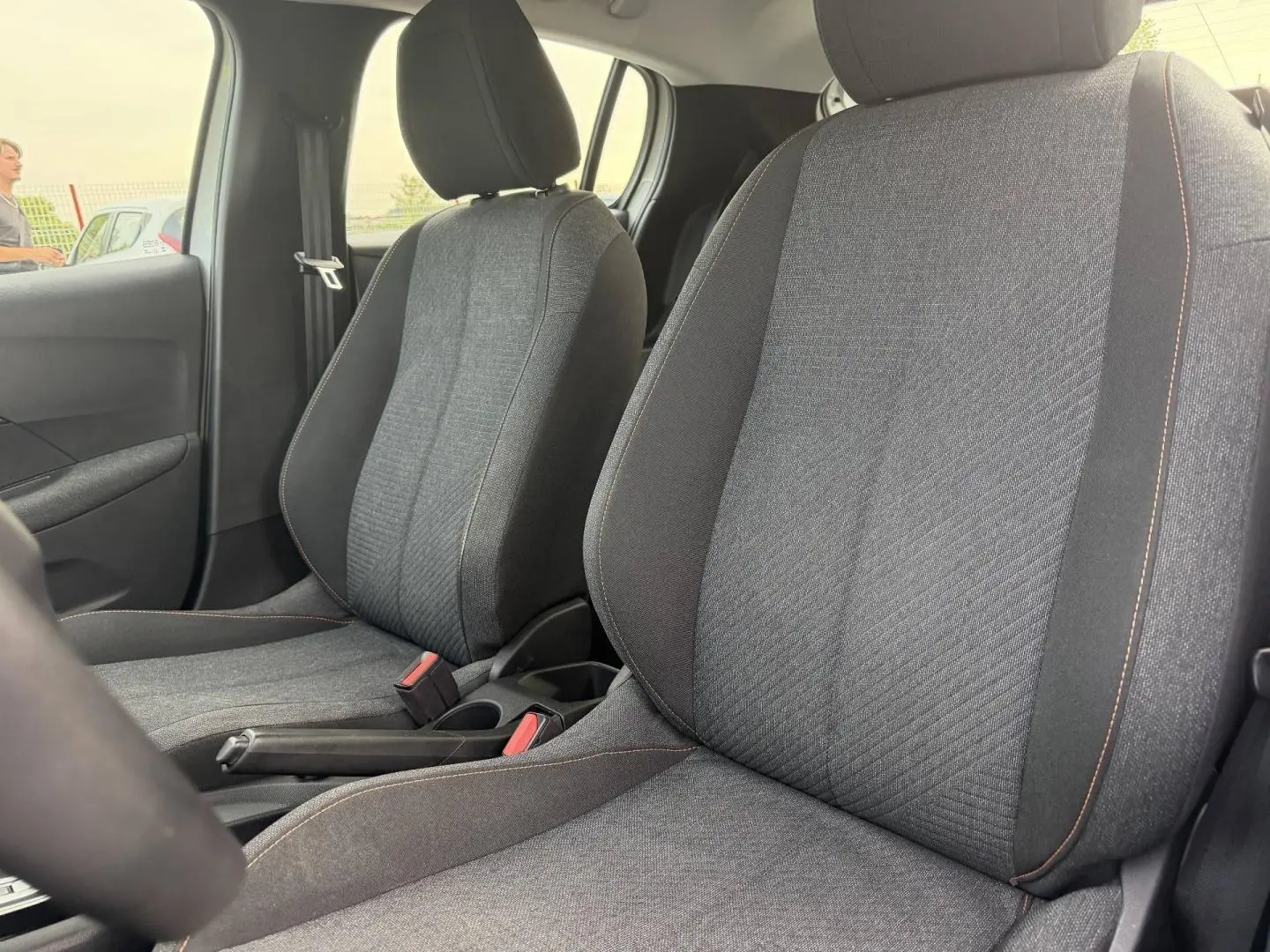 Vue intérieure rapprochée des sièges avant en tissu gris avec surpiqûres orange dans une Peugeot 208 blanche.
