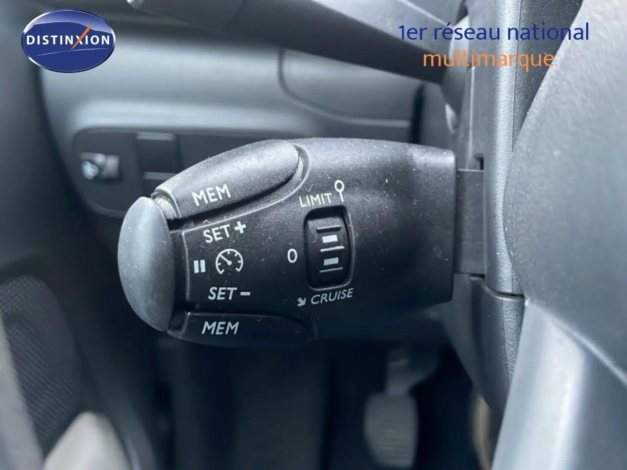 Gros plan sur la commande de régulateur de vitesse noire à gauche du volant d'une Citroën C3 sable métal.