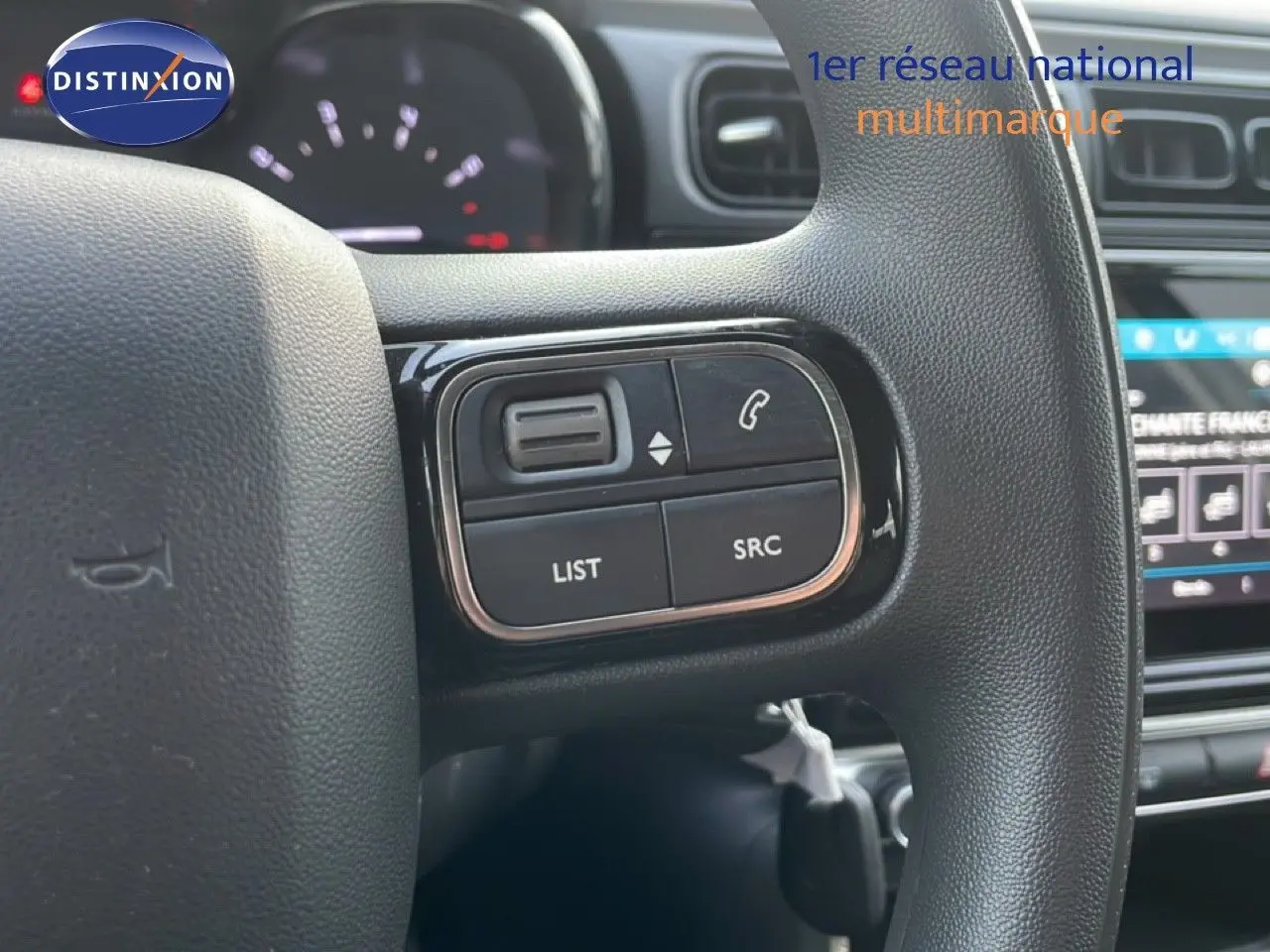 Gros plan sur les commandes au volant noir de la Citroën C3 sable métal, avec tableau de bord et écran tactile en arrière-plan.