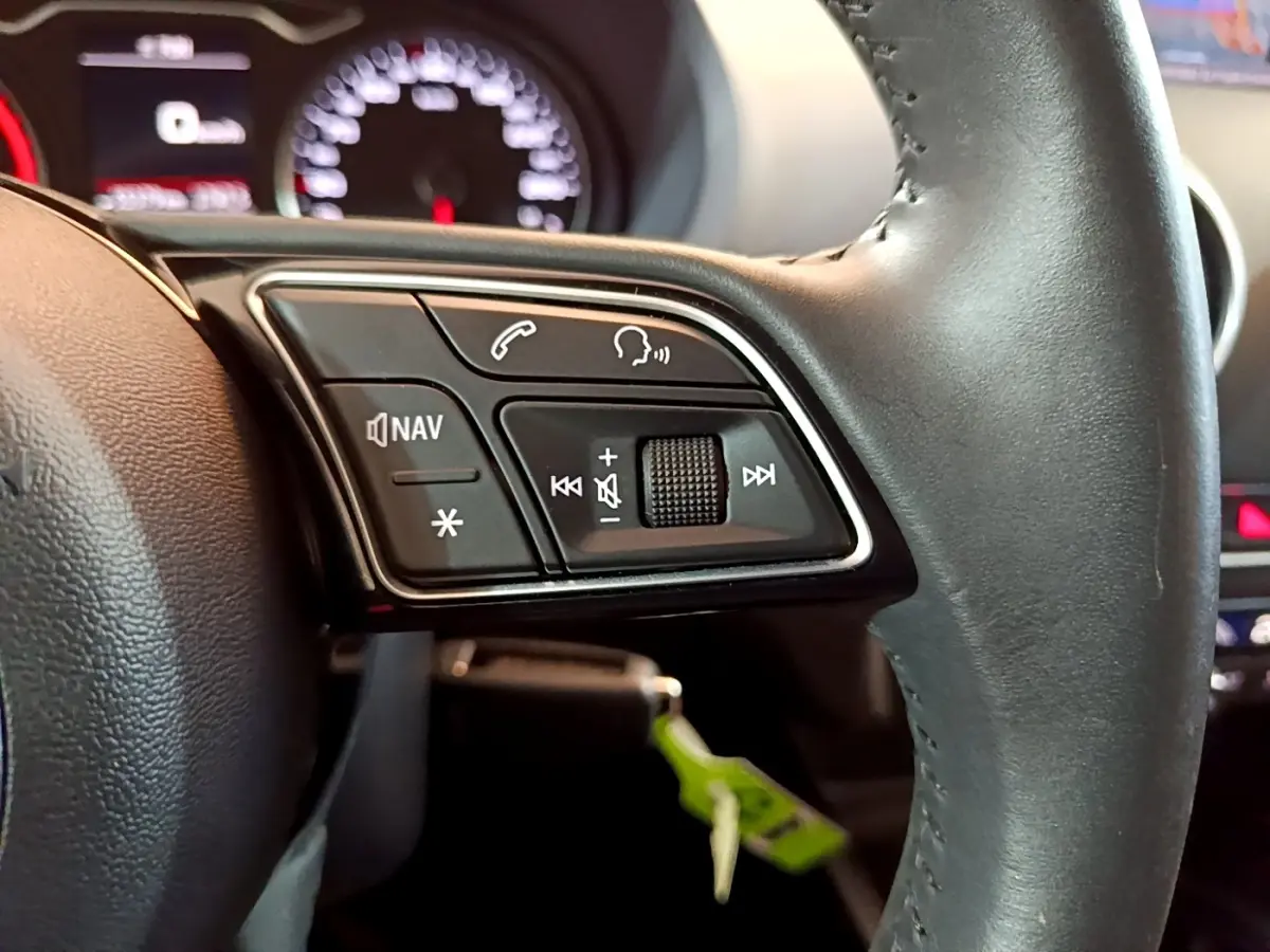 Gros plan sur le volant cuir noir d'une Audi A3 2019, avec commandes multifonctions et tableau de bord flou en arrière-plan.