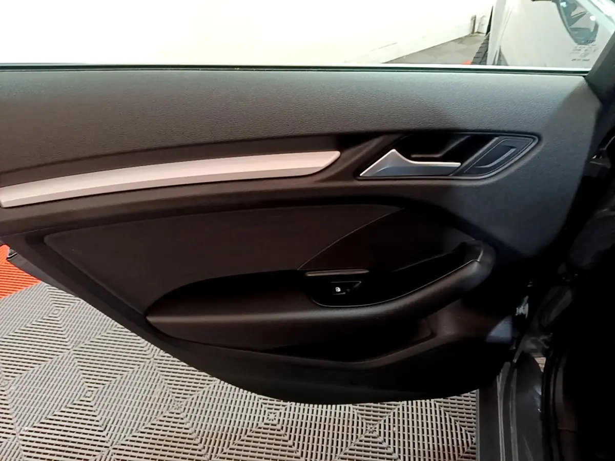 Vue intérieure de la porte avant gauche d'une Audi A3 gris foncé, avec poignée et commande de verrouillage intégrées.