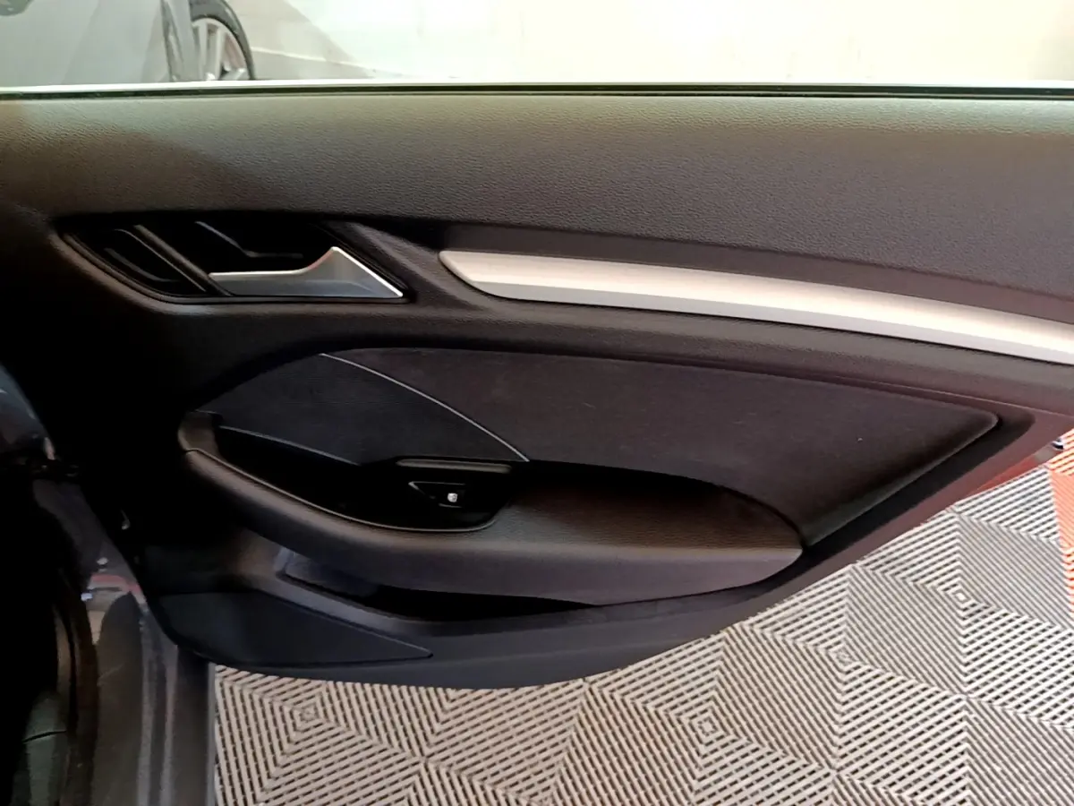 Vue intérieure côté gauche de la porte avant d'une Audi A3 gris foncé avec garniture noire et poignée argentée.