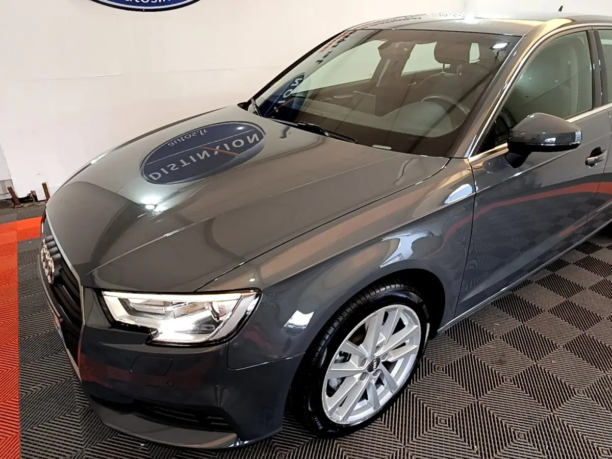 Vue 3/4 avant droit d'une Audi A3 gris foncé brillante avec jantes alliage et phares LED allumés.