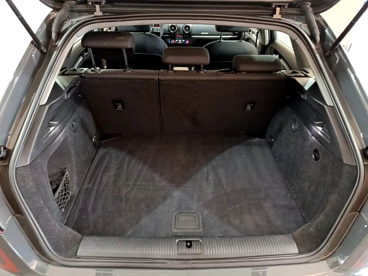 Coffre ouvert vu de l'arrière d'une Audi A3 gris foncé, montrant l'espace de chargement et la banquette arrière.