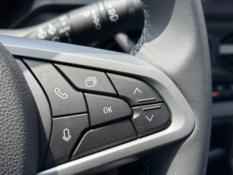 Gros plan sur les commandes multifonctions noires du volant du Dacia Bigster blanc, avec boutons de navigation et appel.
