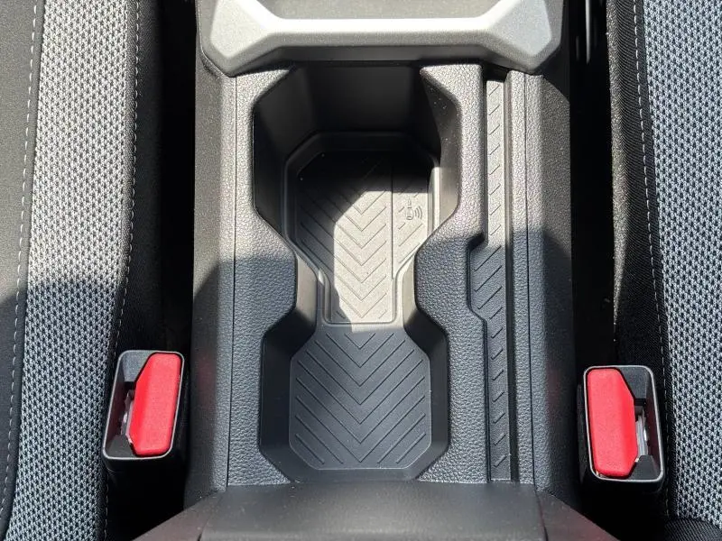 Vue plongeante sur le rangement central noir entre les sièges avant du Dacia Bigster blanc, avec ceintures rouges visibles.