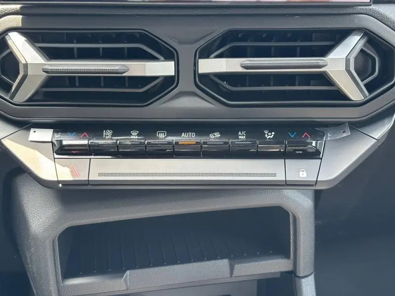 Vue rapprochée de la console centrale du Dacia Bigster blanc, avec commandes climatisation et aérateurs hexagonaux.