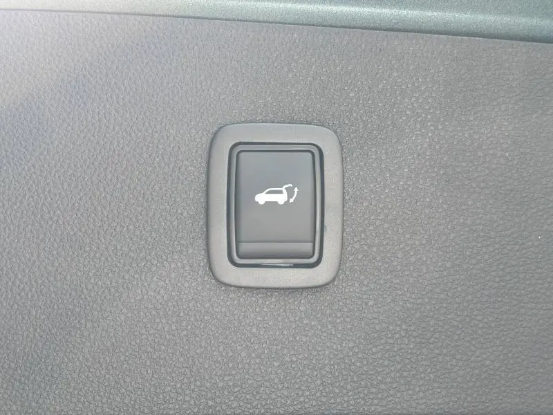 Bouton noir d'ouverture électrique du hayon sur tableau de bord texturé gris du Dacia Bigster blanc.