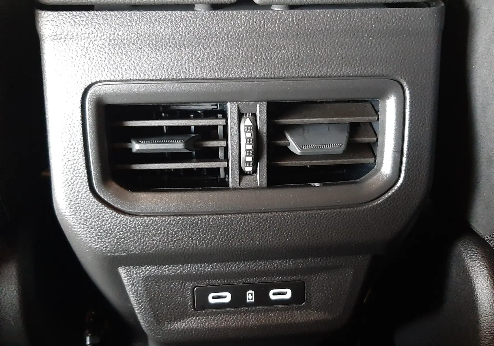 Détail intérieur du Renault Austral 2025, prise d'air arrière noire avec deux ports USB sous accoudoir cuir noir à surpiqûres bleues.