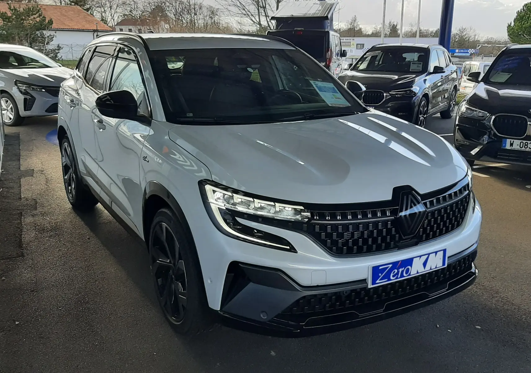 Renault Austral E-Tech blanc nacré avec toit noir, vue 3/4 avant droit sous abri, calandre et phares LED distinctifs.