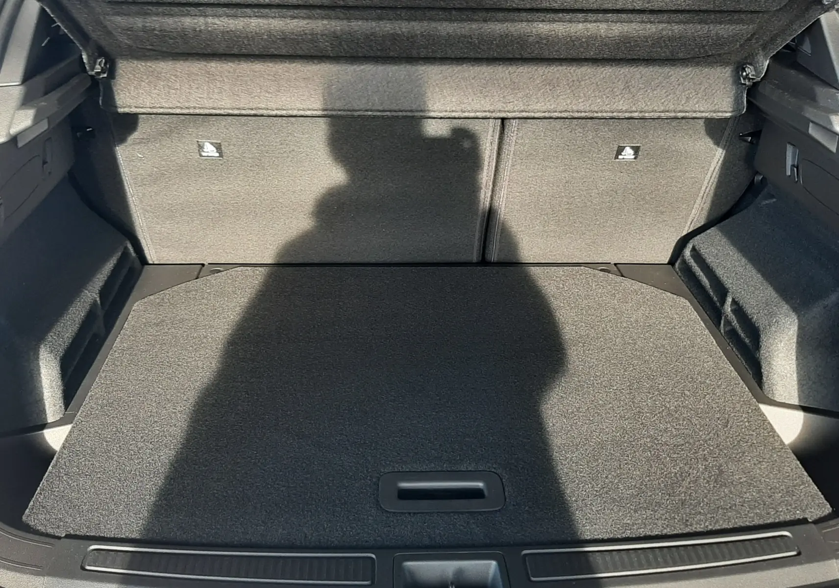 Coffre ouvert vu de l'arrière du Renault Austral blanc nacré, montrant un espace de chargement plat et habillé de moquette grise.