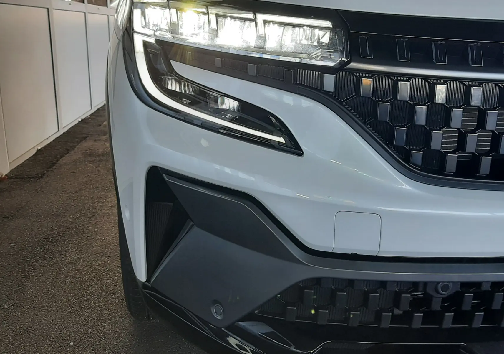 Gros plan sur l’avant gauche du Renault Austral blanc nacré avec toit noir, mettant en valeur les phares LED et la calandre noire.