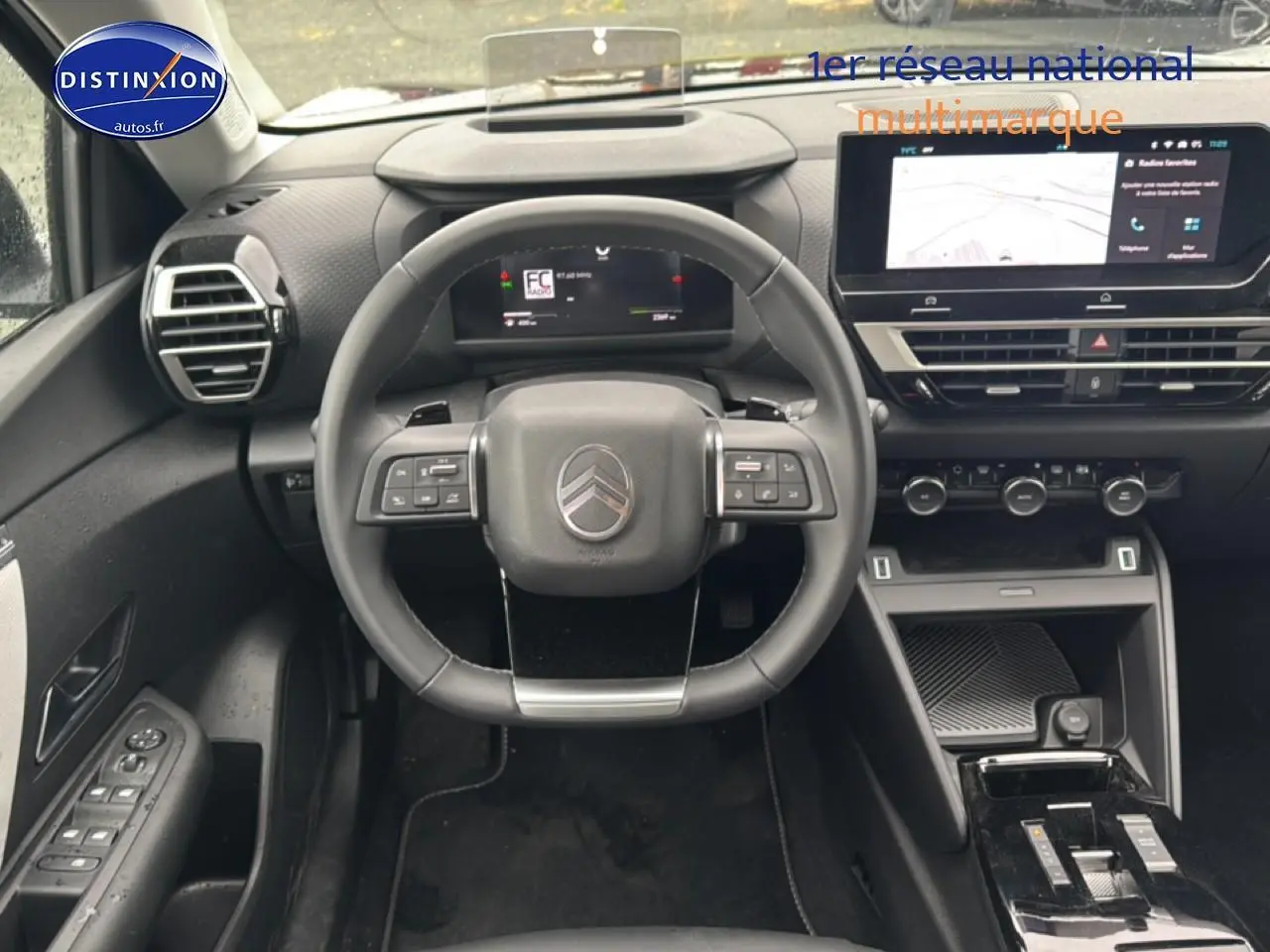 Vue intérieure frontale du poste de conduite noir de la Citroën C4 hybride 2025 avec écran tactile et volant multifonction.