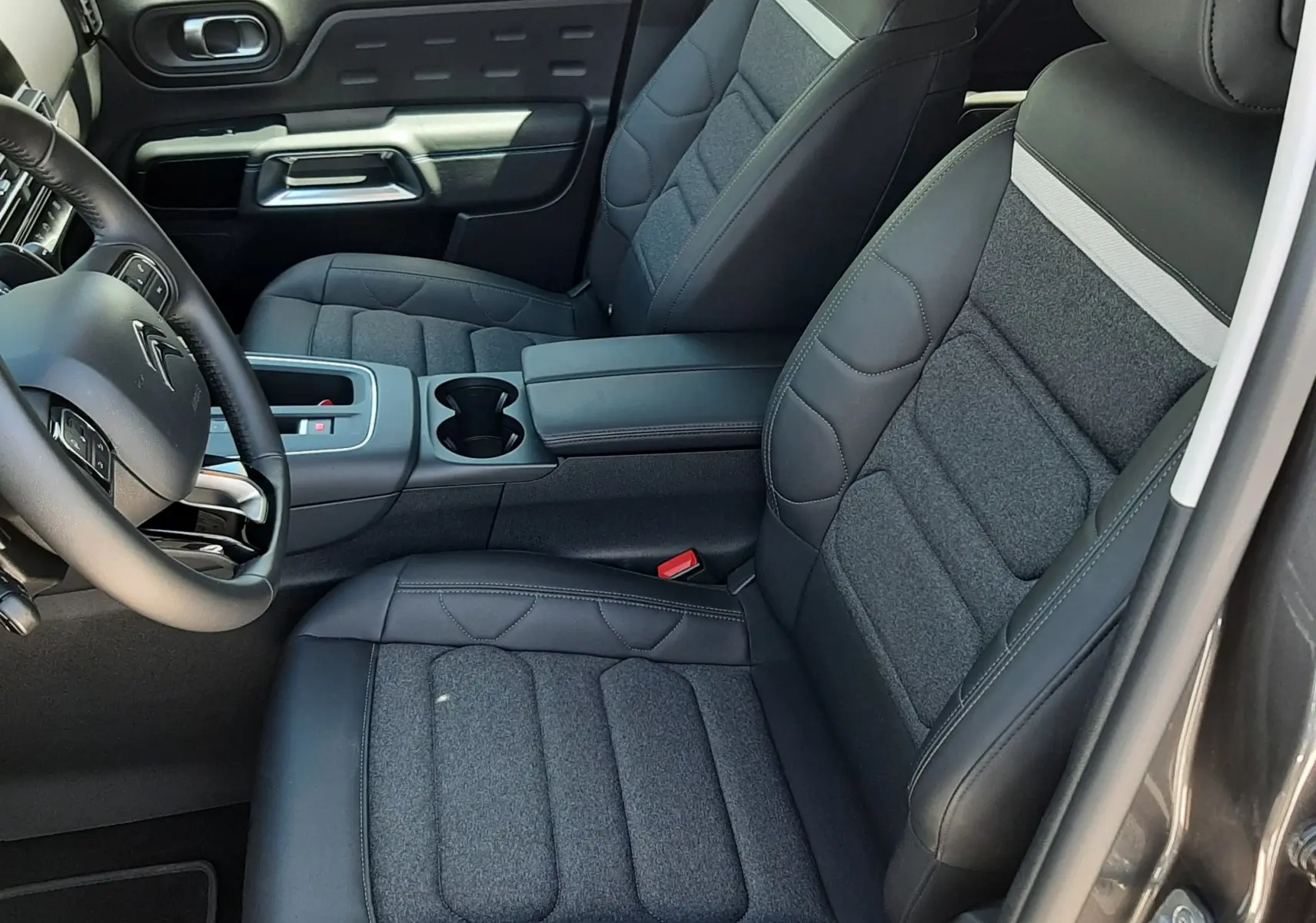 Vue intérieure côté conducteur du Citroën C5 Aircross hybride 2025, sièges tissu et cuir noir avec surpiqûres grises.