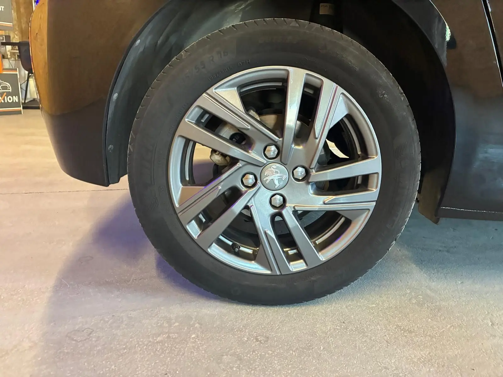 Gros plan sur la roue avant gauche d'une Peugeot 208 noire, mettant en valeur la jante alliage au design moderne.