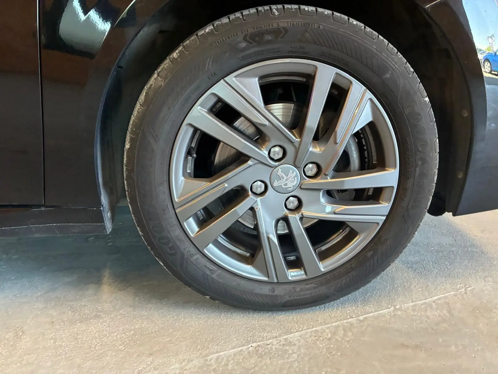 Gros plan sur la roue avant droite d'une Peugeot 208 noire 2021, mettant en valeur la jante alliage au design moderne.