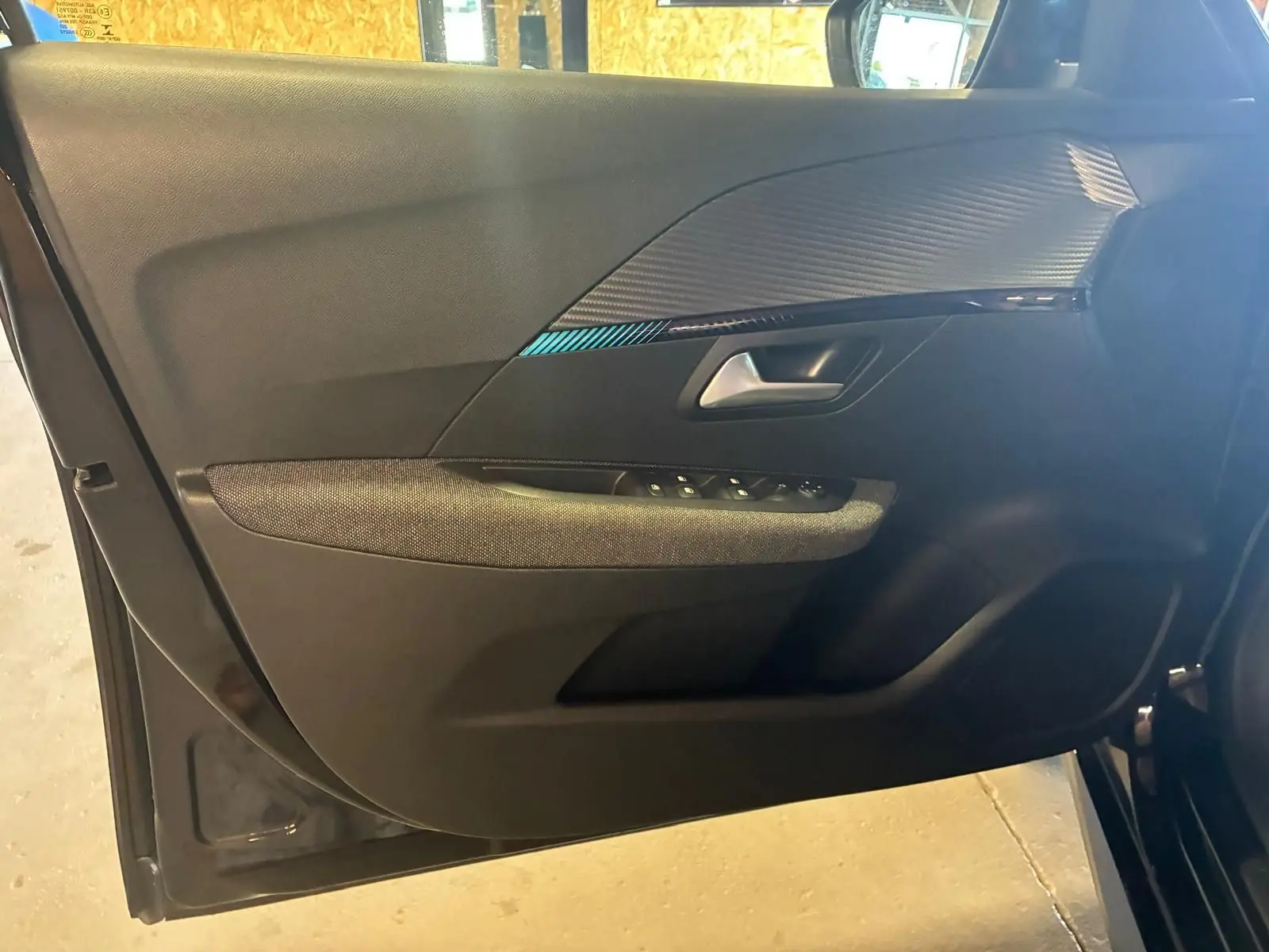Vue intérieure de la porte côté gauche d'une Peugeot 208 noire, avec garniture tissu et inserts décoratifs noirs.