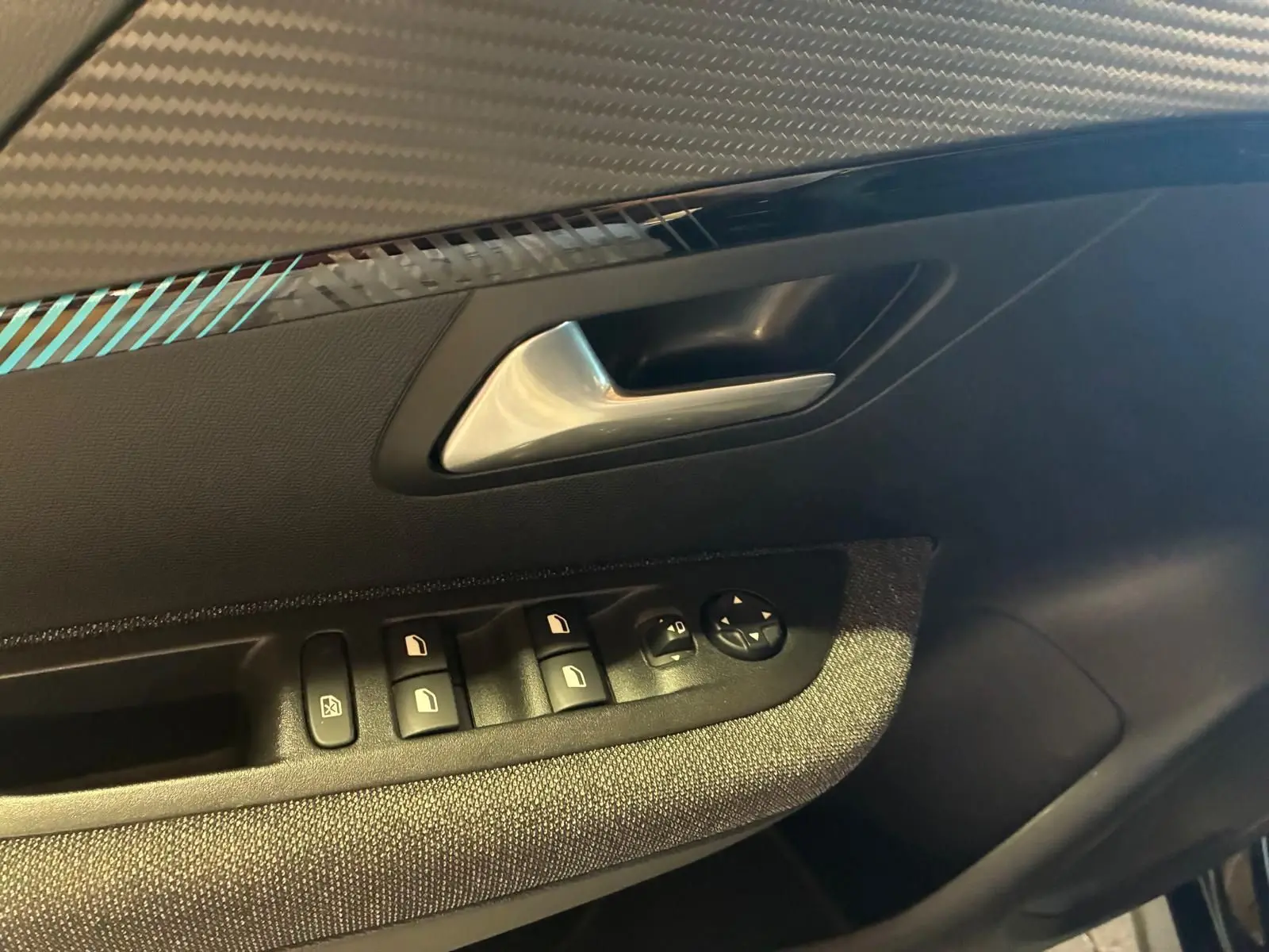 Gros plan sur la poignée intérieure côté gauche de la porte d’une Peugeot 208 noire avec commandes des vitres et rétroviseurs.