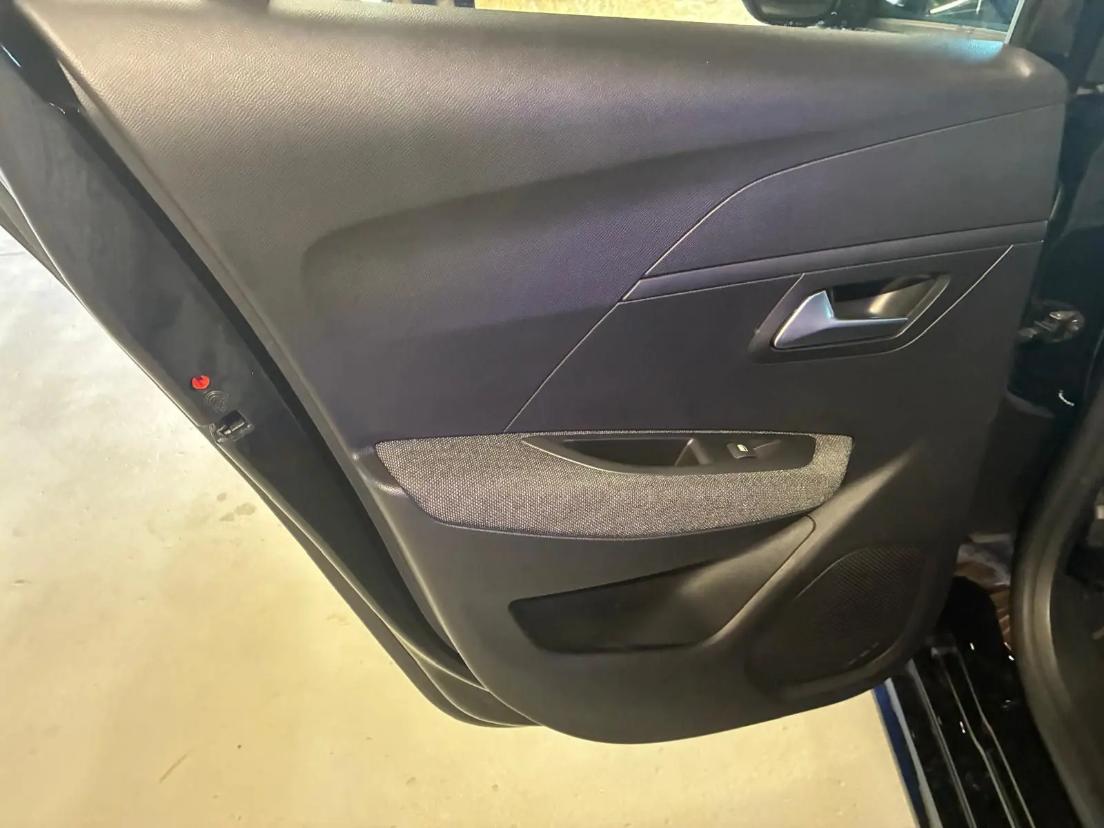 Vue rapprochée de la porte arrière gauche intérieure noire de la Peugeot 208 1.5 BlueHDi 100 Style avec tissu gris.