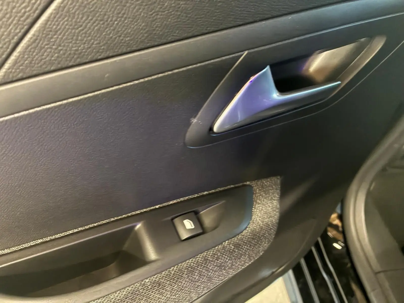 Détail de la porte intérieure côté gauche de la Peugeot 208 noire, avec poignée argentée et commande de vitre électrique.