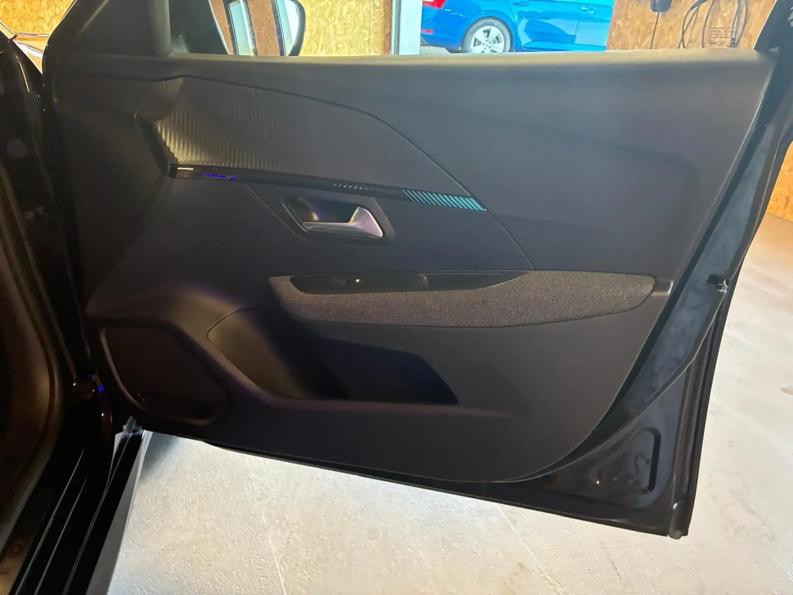 Vue intérieure de la porte avant gauche noire d'une Peugeot 208 1.5 BlueHDi 100 Style avec garniture tissu et plastique.