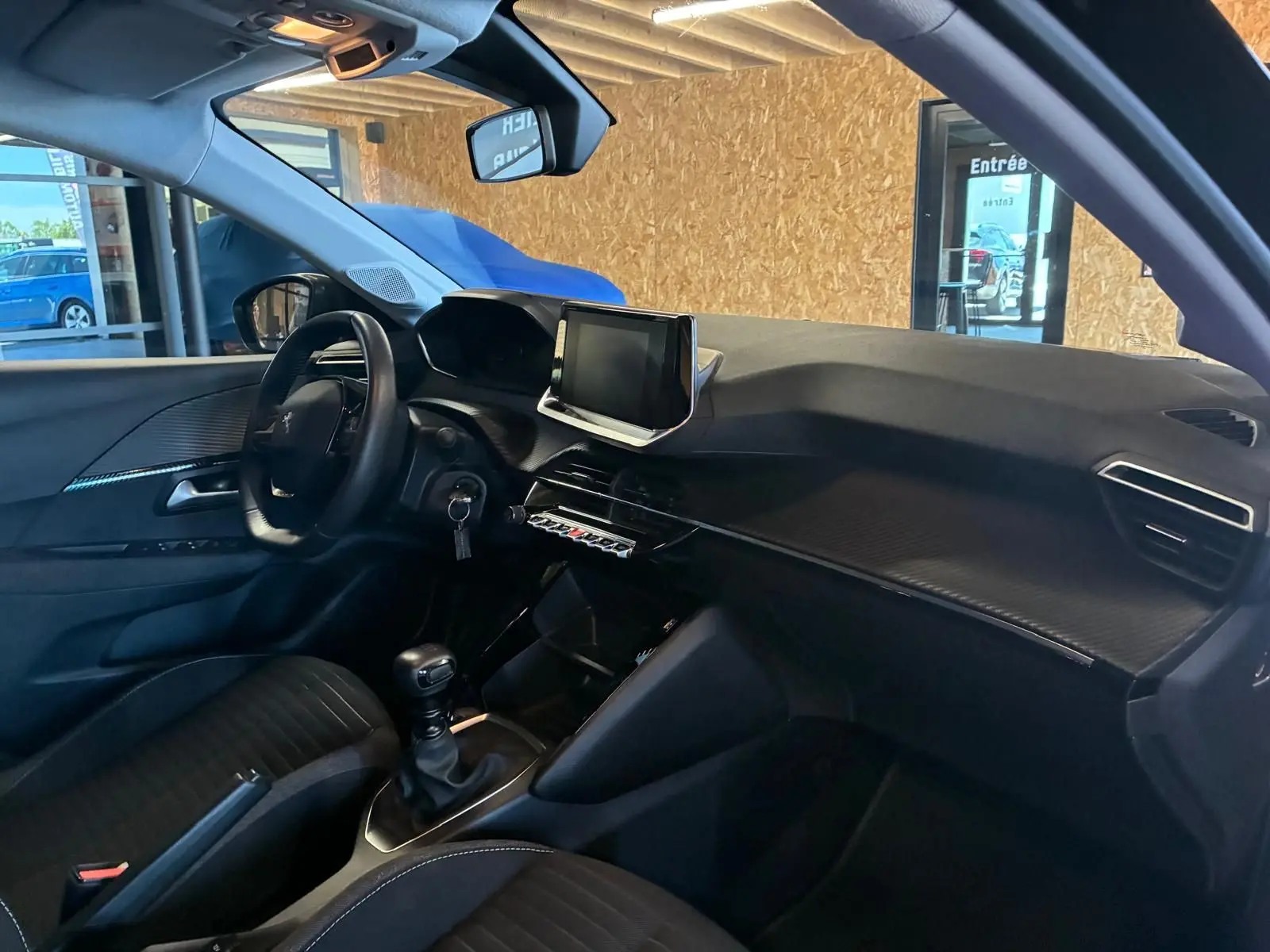 Vue intérieure côté conducteur de la Peugeot 208 1.5 BlueHDi 100 Style 2021 avec tableau de bord noir et écran tactile central.