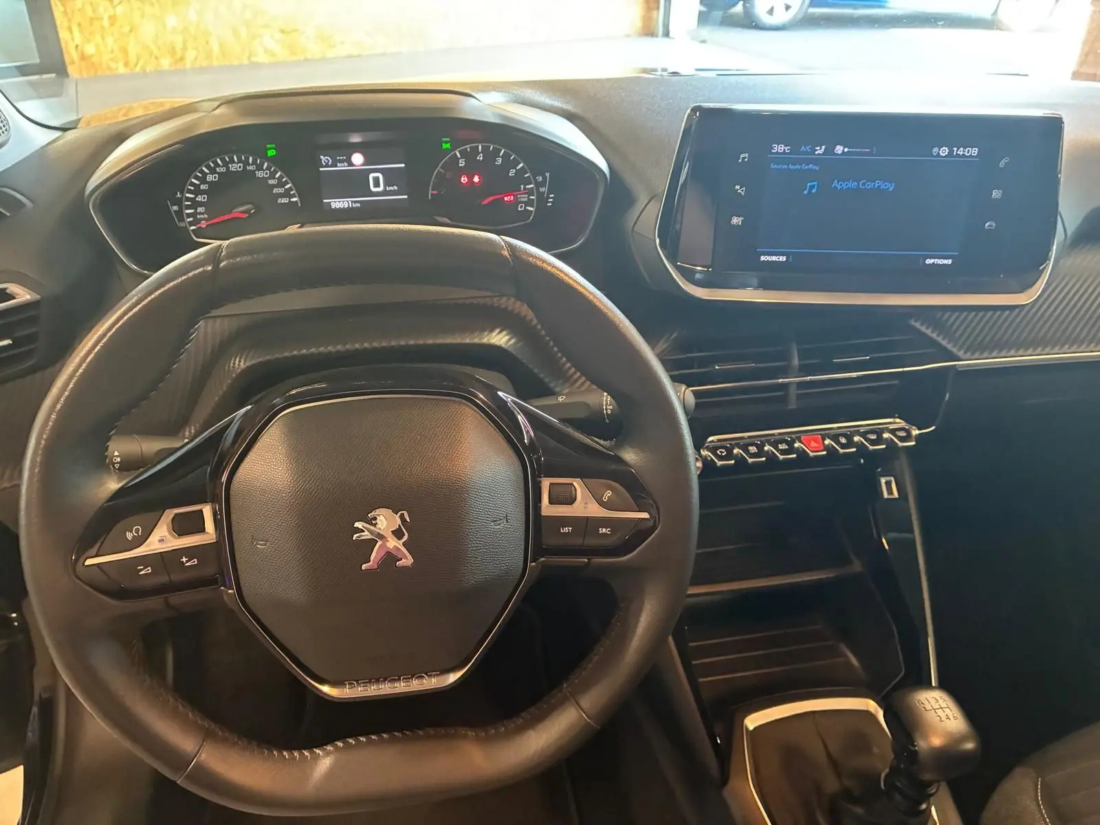 Vue intérieure centrée sur le volant et le tableau de bord de la Peugeot 208 noire avec écran tactile et boîte manuelle.