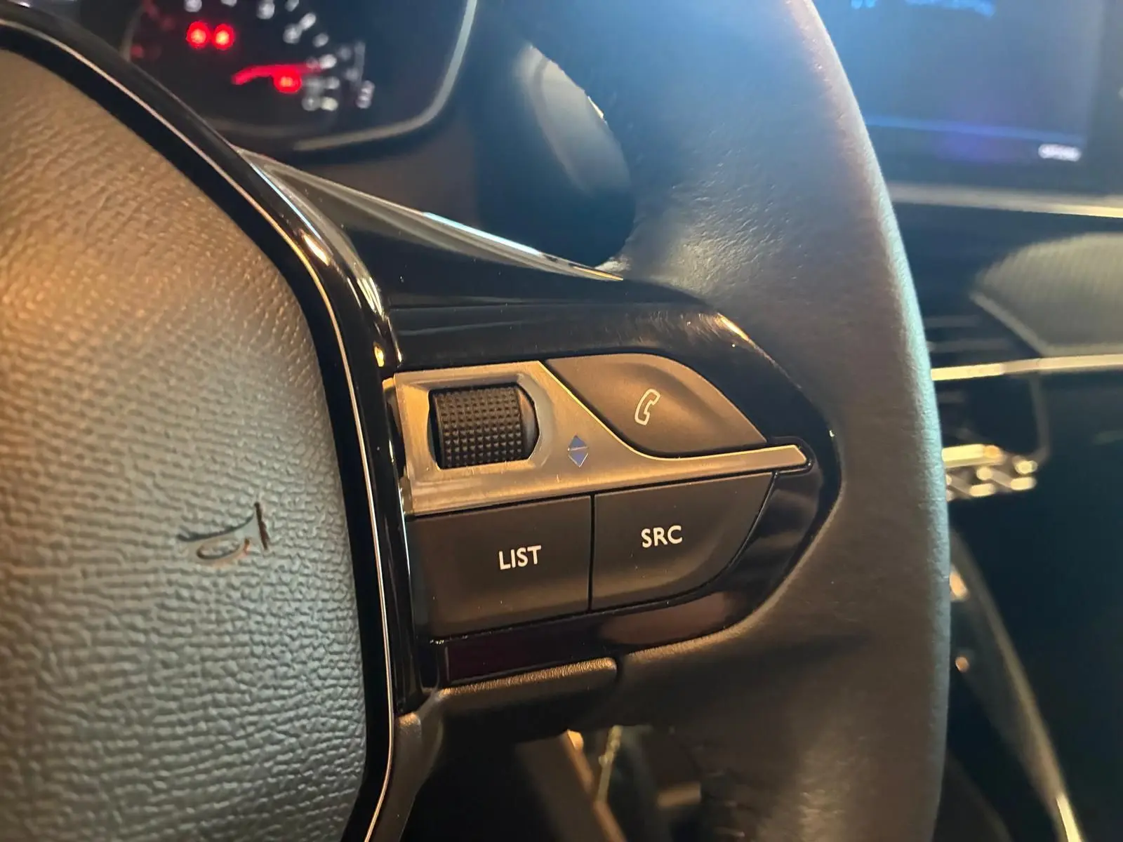 Gros plan sur les commandes gauche du volant noir de la Peugeot 208 1.5 BlueHDi 100 Style, avec boutons LIST et SRC visibles.