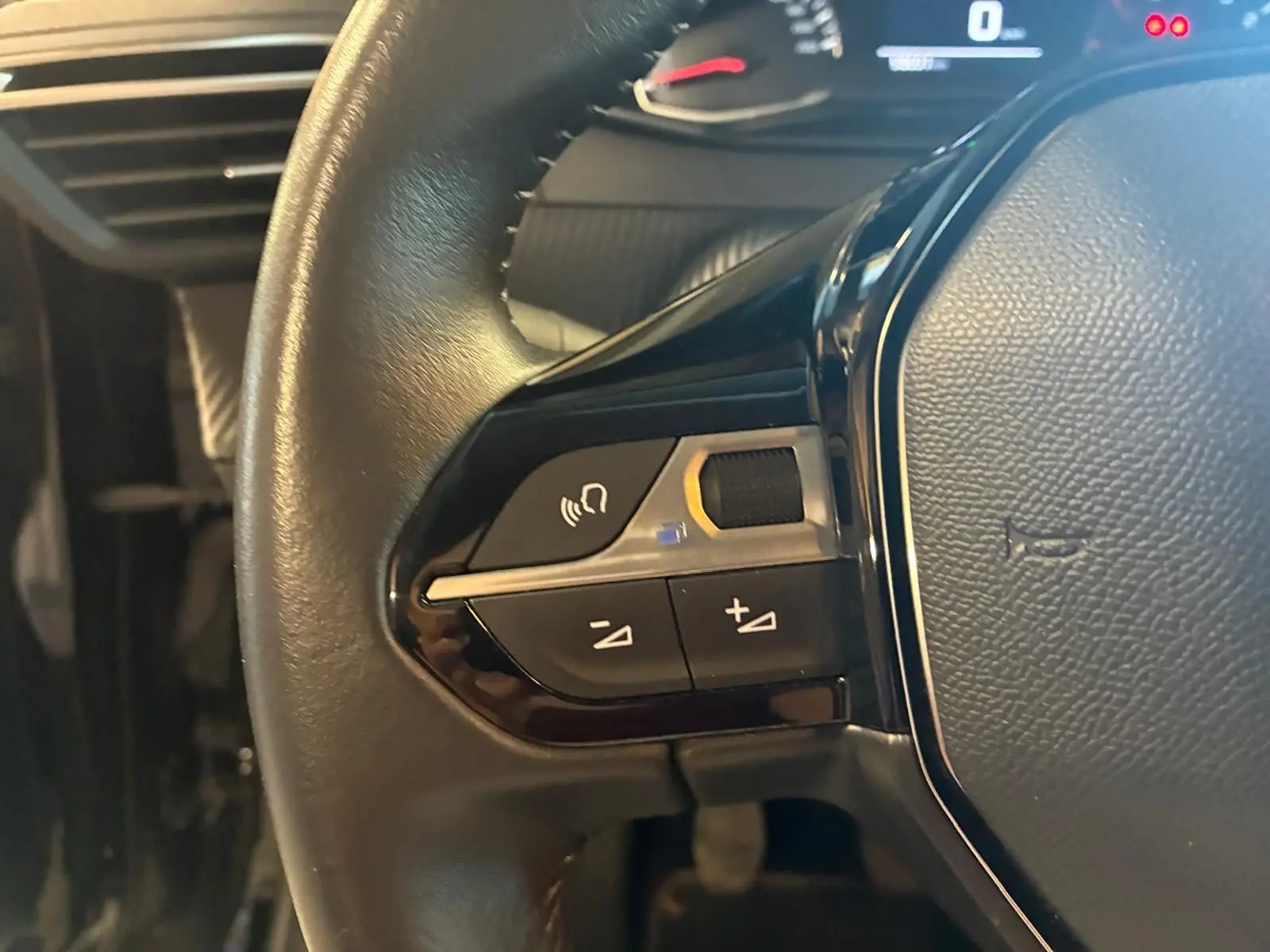 Gros plan sur les commandes gauche du volant noir de la Peugeot 208 1.5 BlueHDi 100 Style, tableau de bord en arrière-plan.