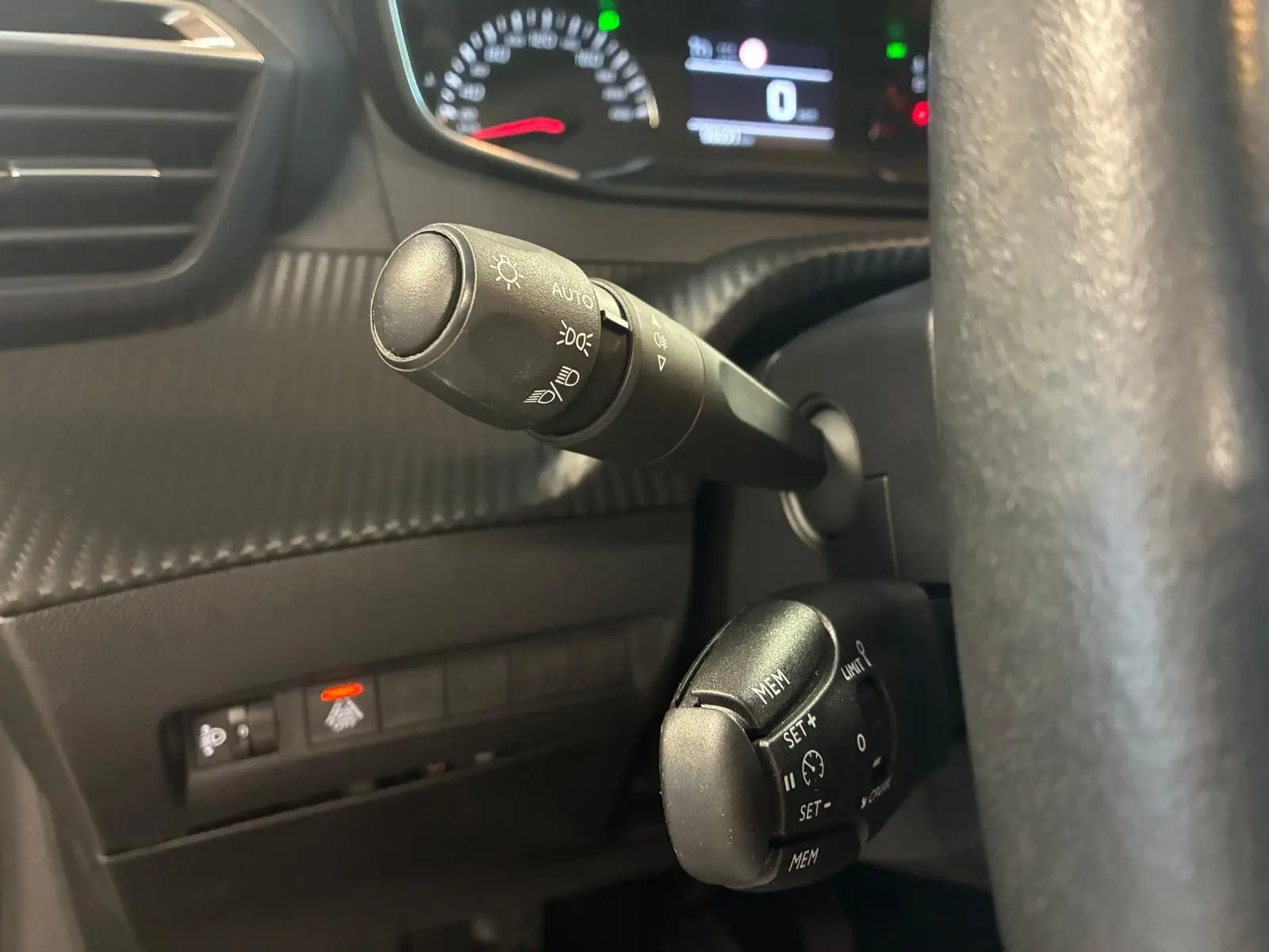 Gros plan sur les commandes de phares et régulateur de vitesse du tableau de bord noir d’une Peugeot 208 1.5 BlueHDi 100 Style 2021.