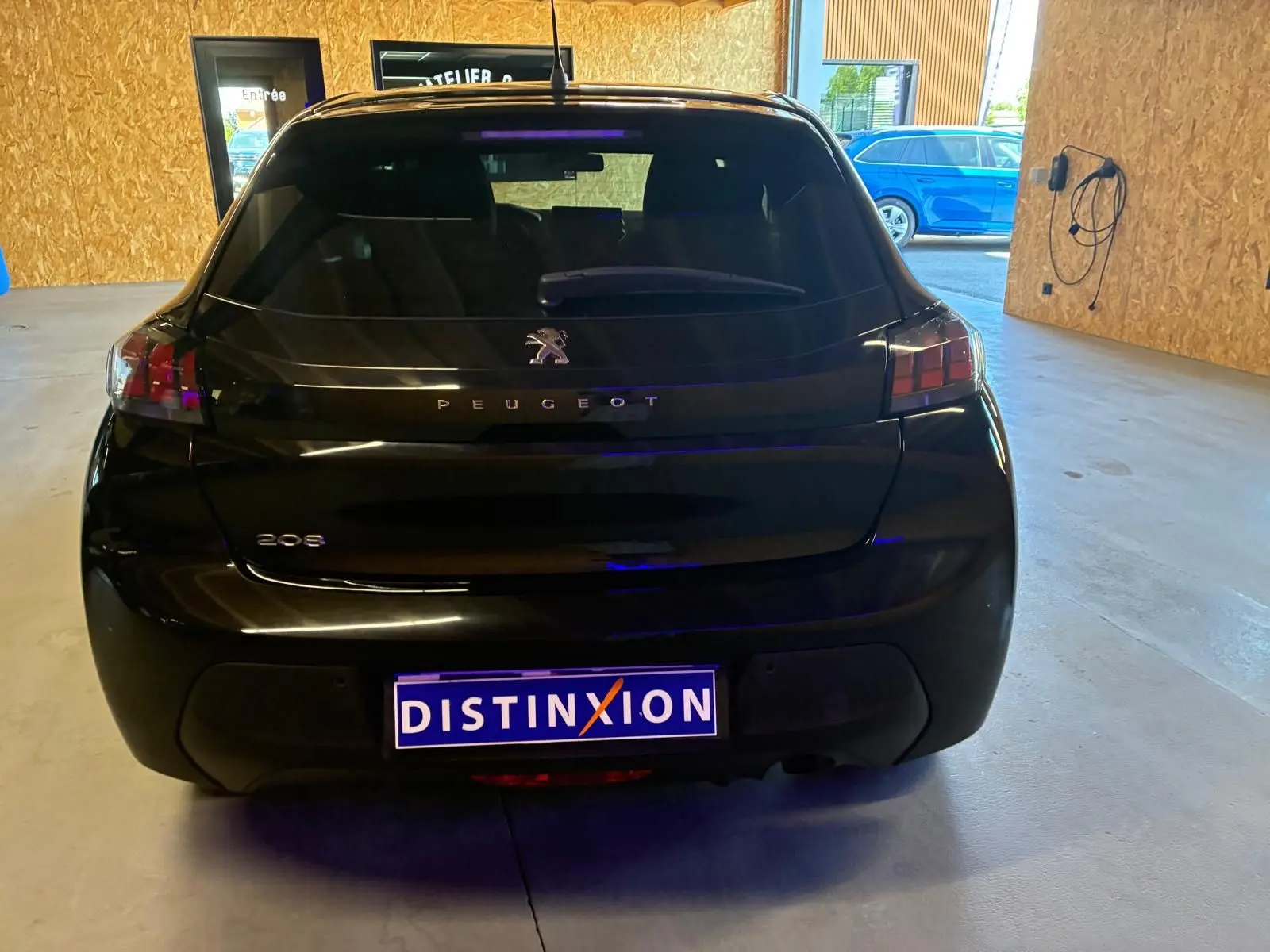 Vue arrière d'une Peugeot 208 noire 2021, avec logo et plaques distinctives visibles en intérieur d'atelier.