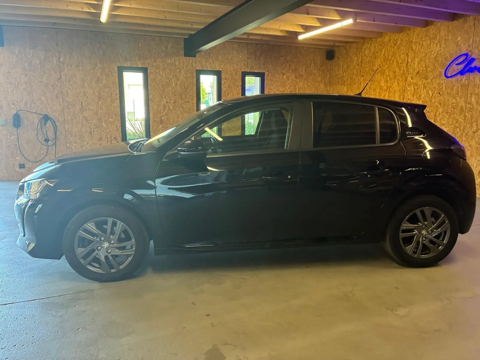 Profil côté gauche d'une Peugeot 208 noire 5 portes, version 1.5 BlueHDi 100 Style, stationnée en intérieur.