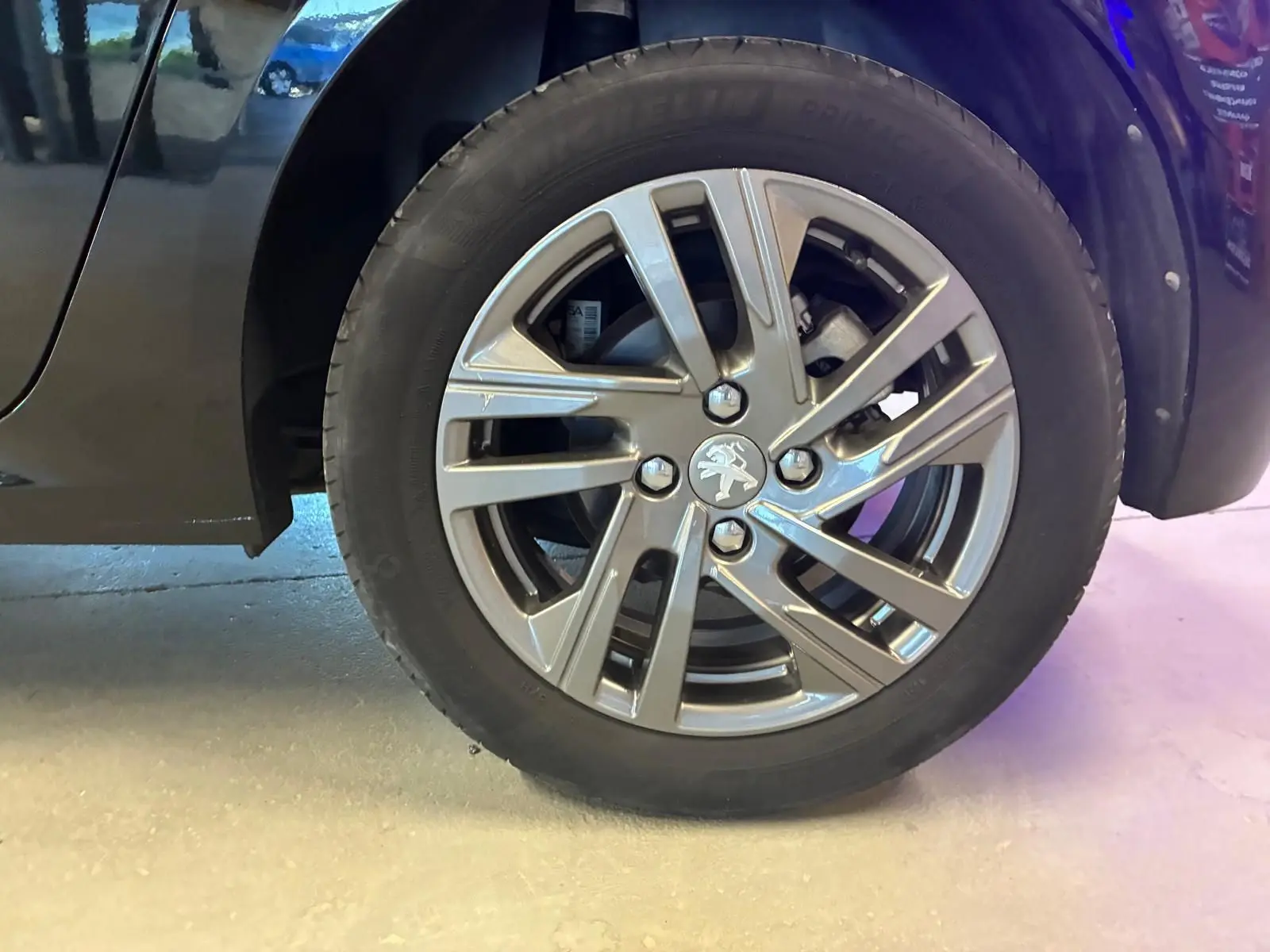 Gros plan sur la roue avant droite noire d'une Peugeot 208 1.5 BlueHDi 100 Style avec jante alliage grise.