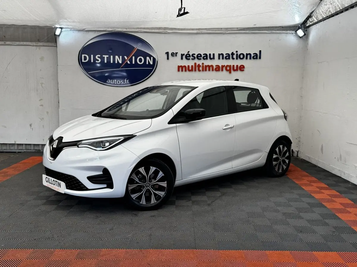 Renault ZOE Iconic R135 blanc vue 3/4 avant droit, avec jantes spécifiques et phares LED allumés.