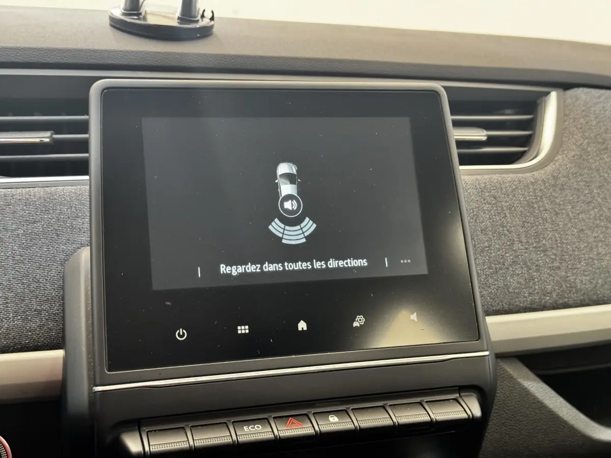 Écran tactile central affichant l'aide au stationnement dans l'habitacle d'une Renault ZOE blanche, vue de face.