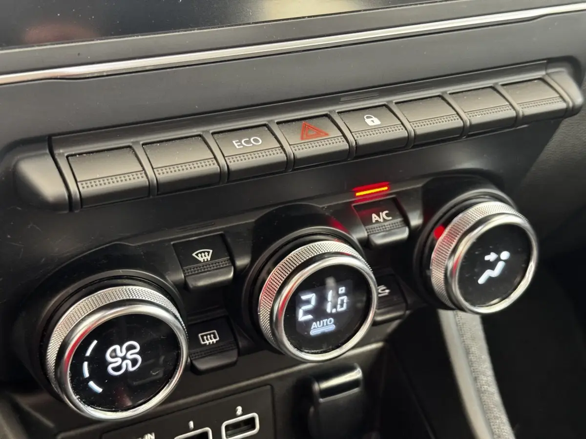 Gros plan sur les commandes de climatisation et boutons multifonctions noirs du tableau de bord de la Renault ZOE blanche.