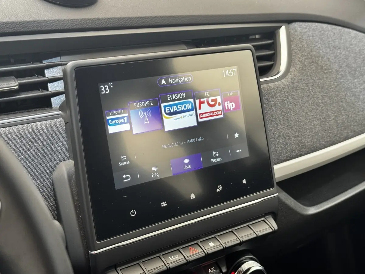 Écran tactile central affichant la radio dans l’habitacle sombre d’une Renault ZOE blanche Iconic R135 vue de face.