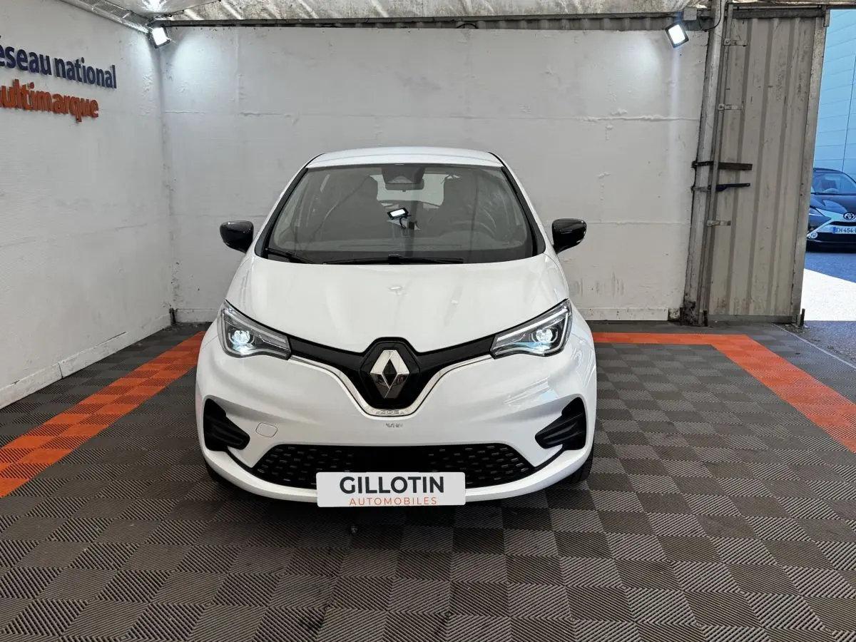 Renault ZOE Iconic R135 blanc vue de face en intérieur, phares LED allumés et calandre noire distinctive.