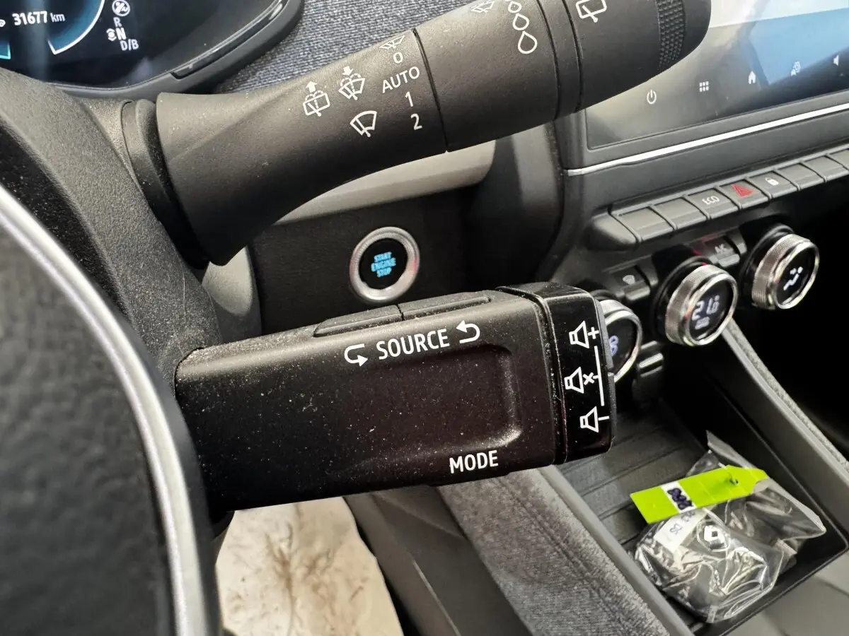 Gros plan sur la commande multimédia au volant d’une Renault ZOE blanche, avec tableau de bord et bouton démarrage visibles.